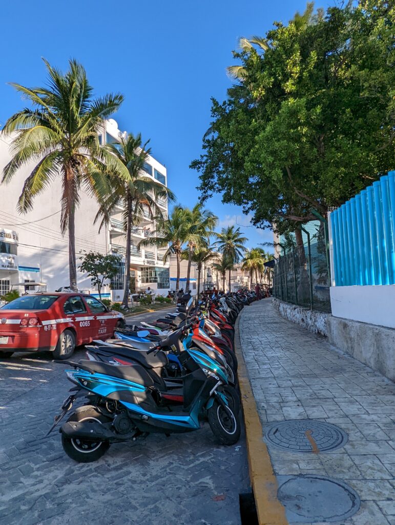 a row of scooters parked along a main street in Isla Mujeres, Mexico